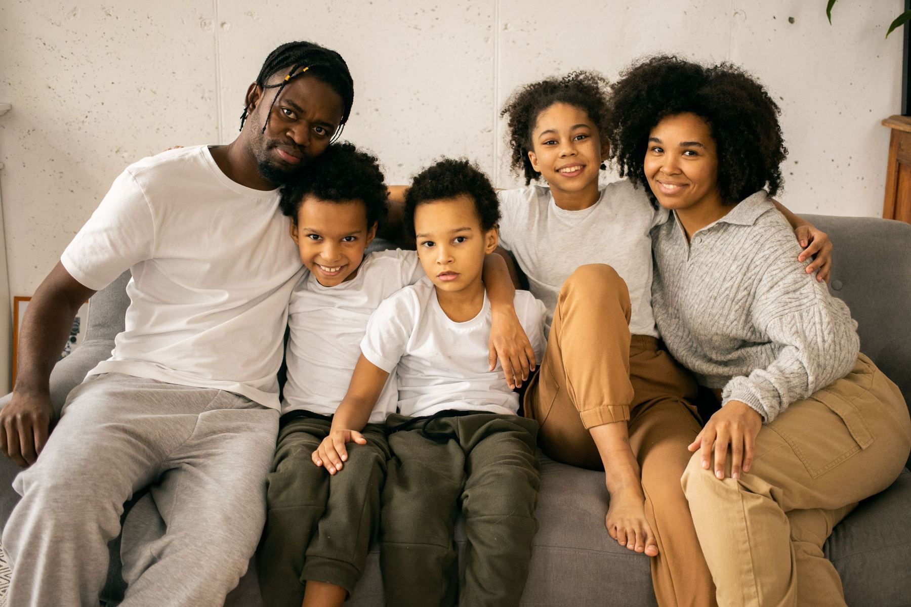 A mother, a father and their three children sitting close together on a sofa at home